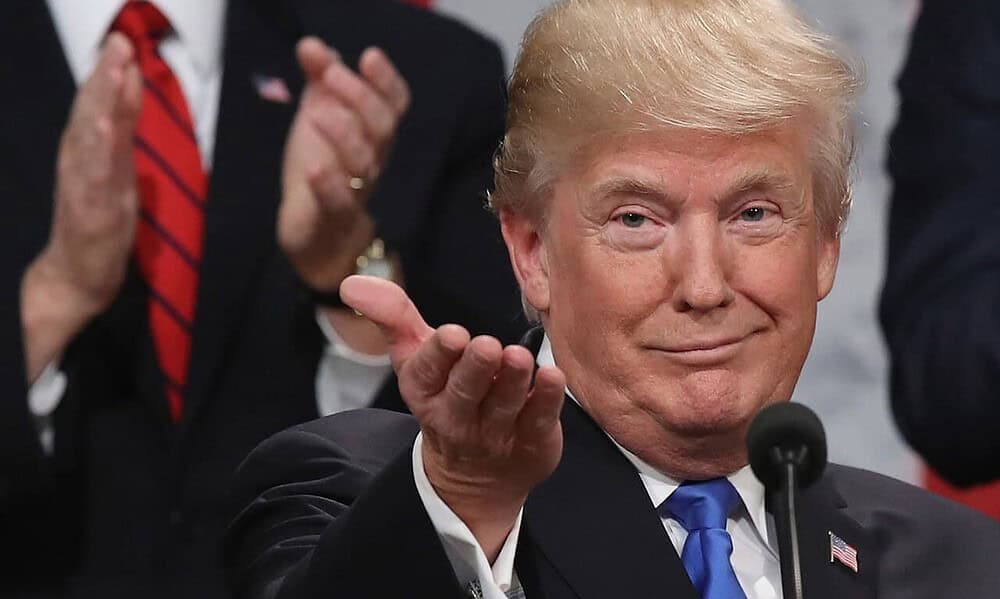 Person gesturing with hand, crowd clapping behind.