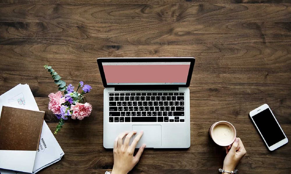 person using apple computer while drinking coffee at wooden desk