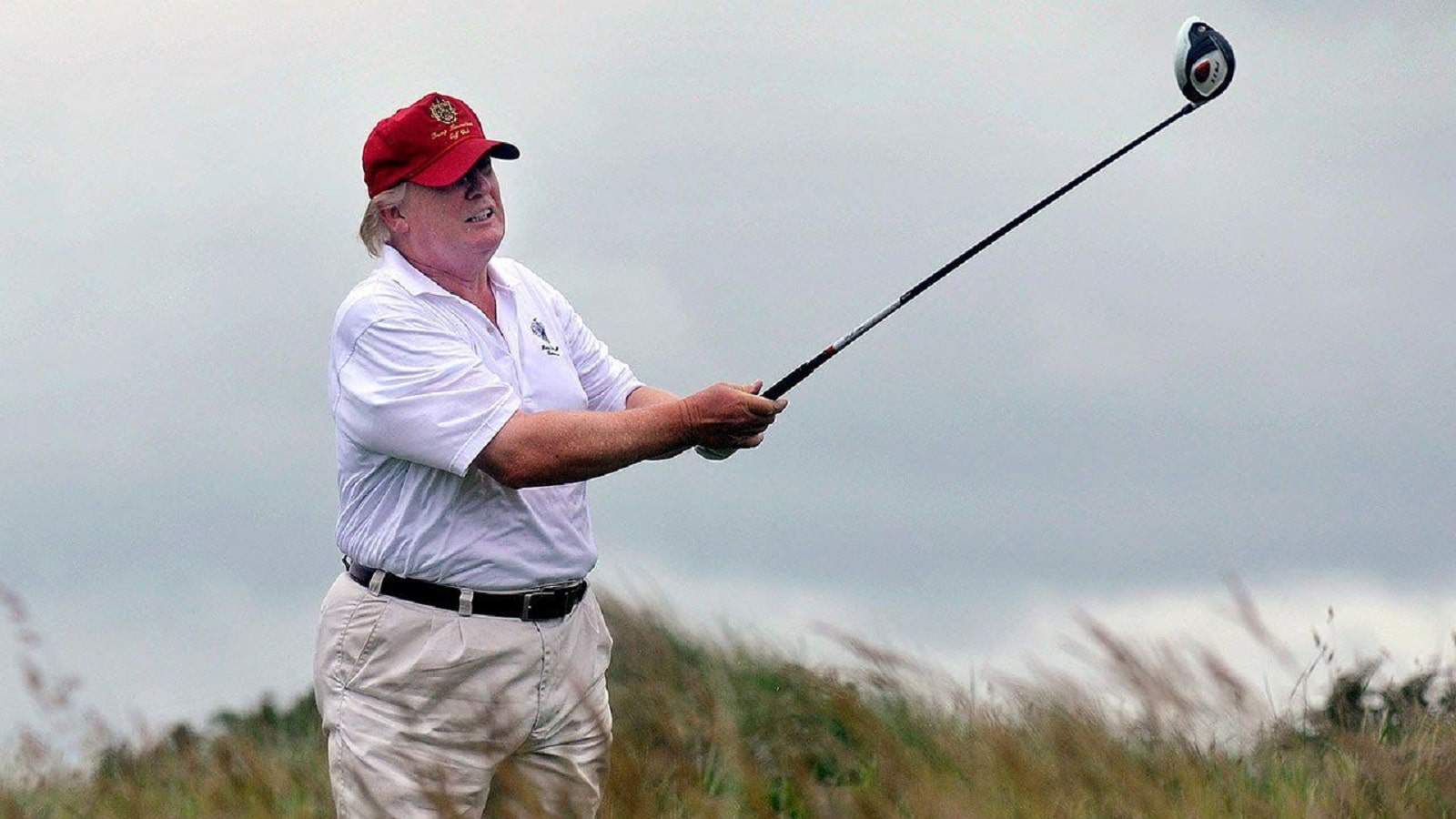 Man playing golf with red cap outdoors.