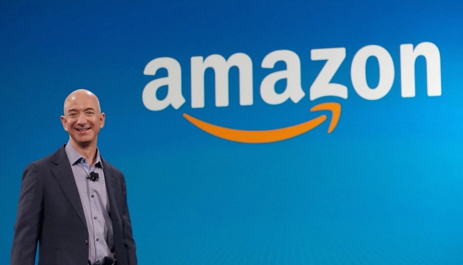 amazon logo behind a standing jeff bezos