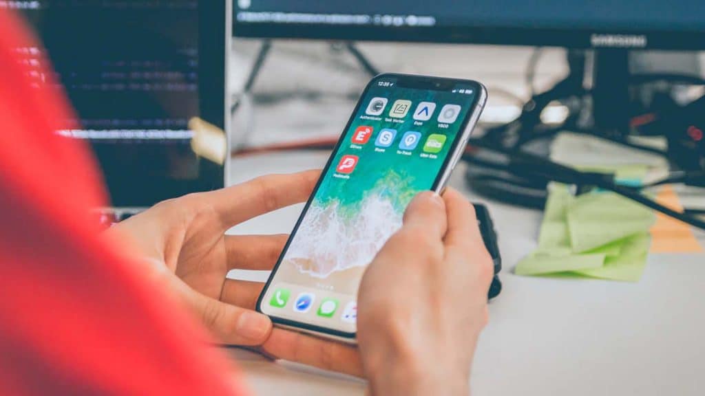 person holding iphone at desk using facebook