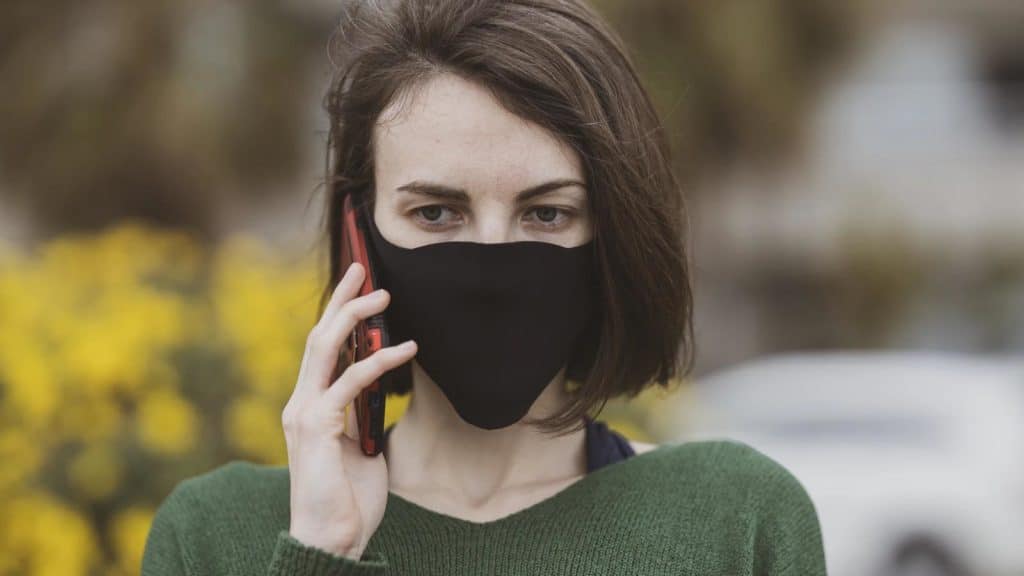 person wearing covid-19 mask and talking on smartphone