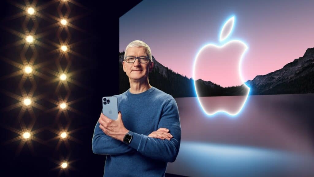 Apple ceo tim cook standing on stage holding an iphone while wearing an apple watch