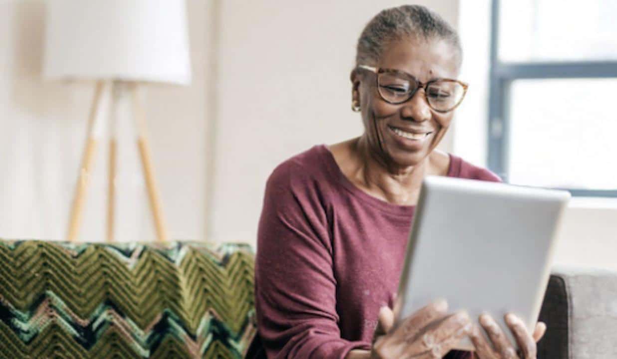 senior citizen holding an ipad sitting on a couch