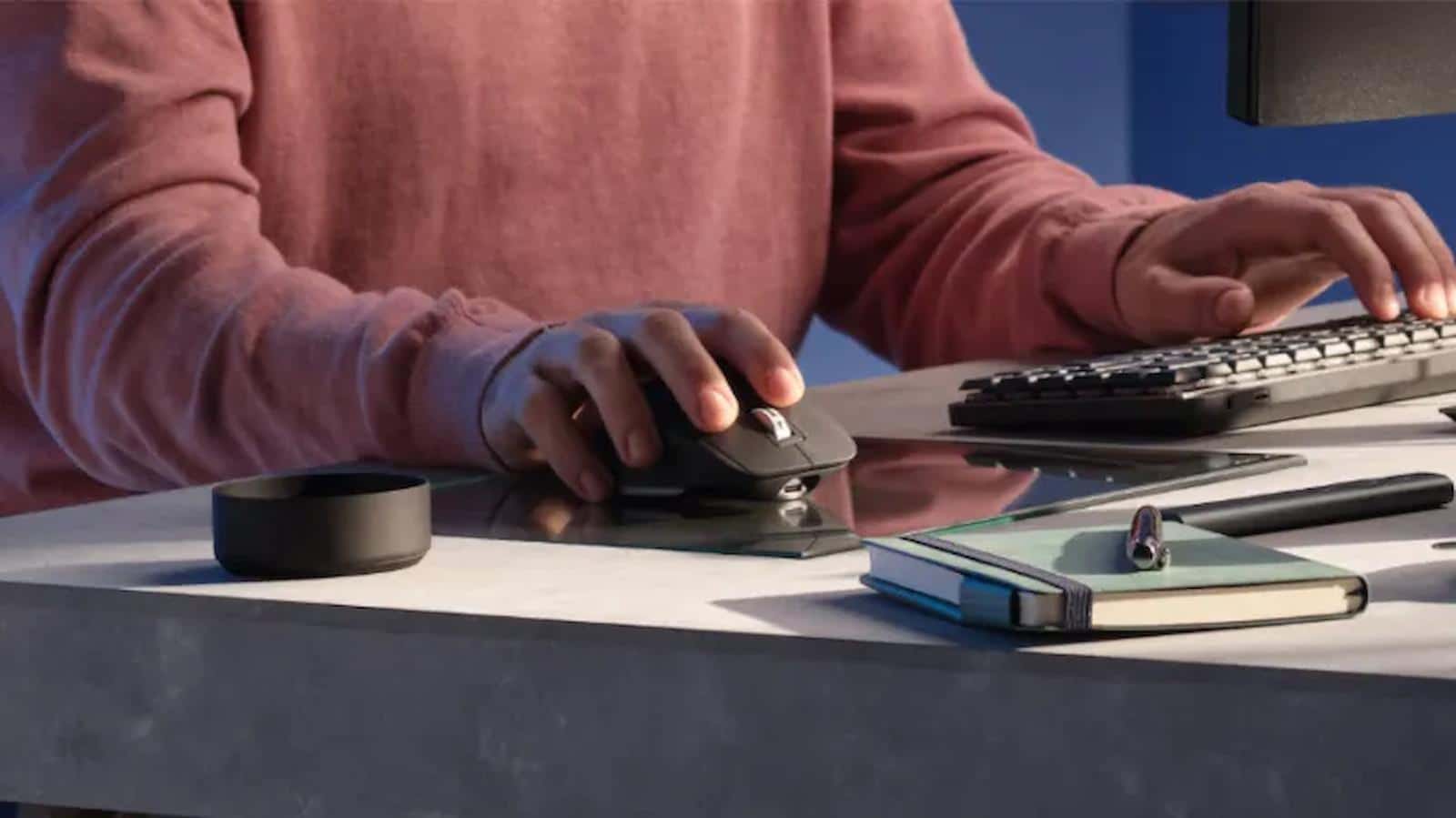 logitech mx master 3s mouse and mx mechanical keyboard on a desk being used by a black-skinned man in a red sweater