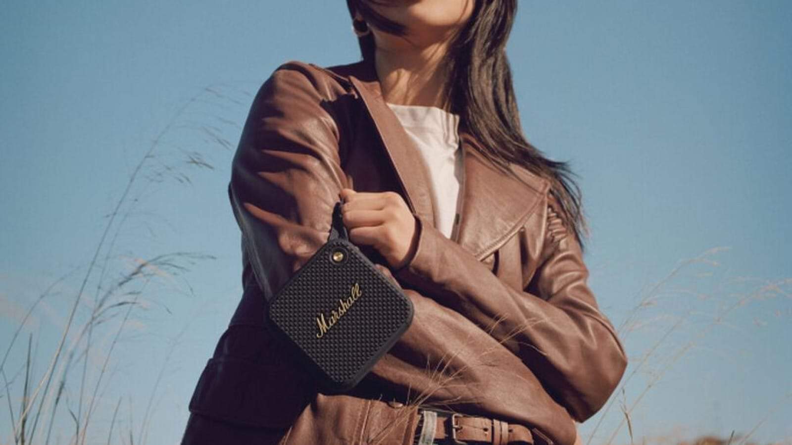 Marshall willen bluetooth speaker held in the hand of a woman wearing a brown leather jacket