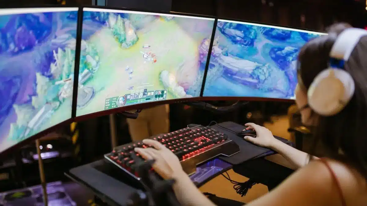 person playing a PC game with three monitors in front