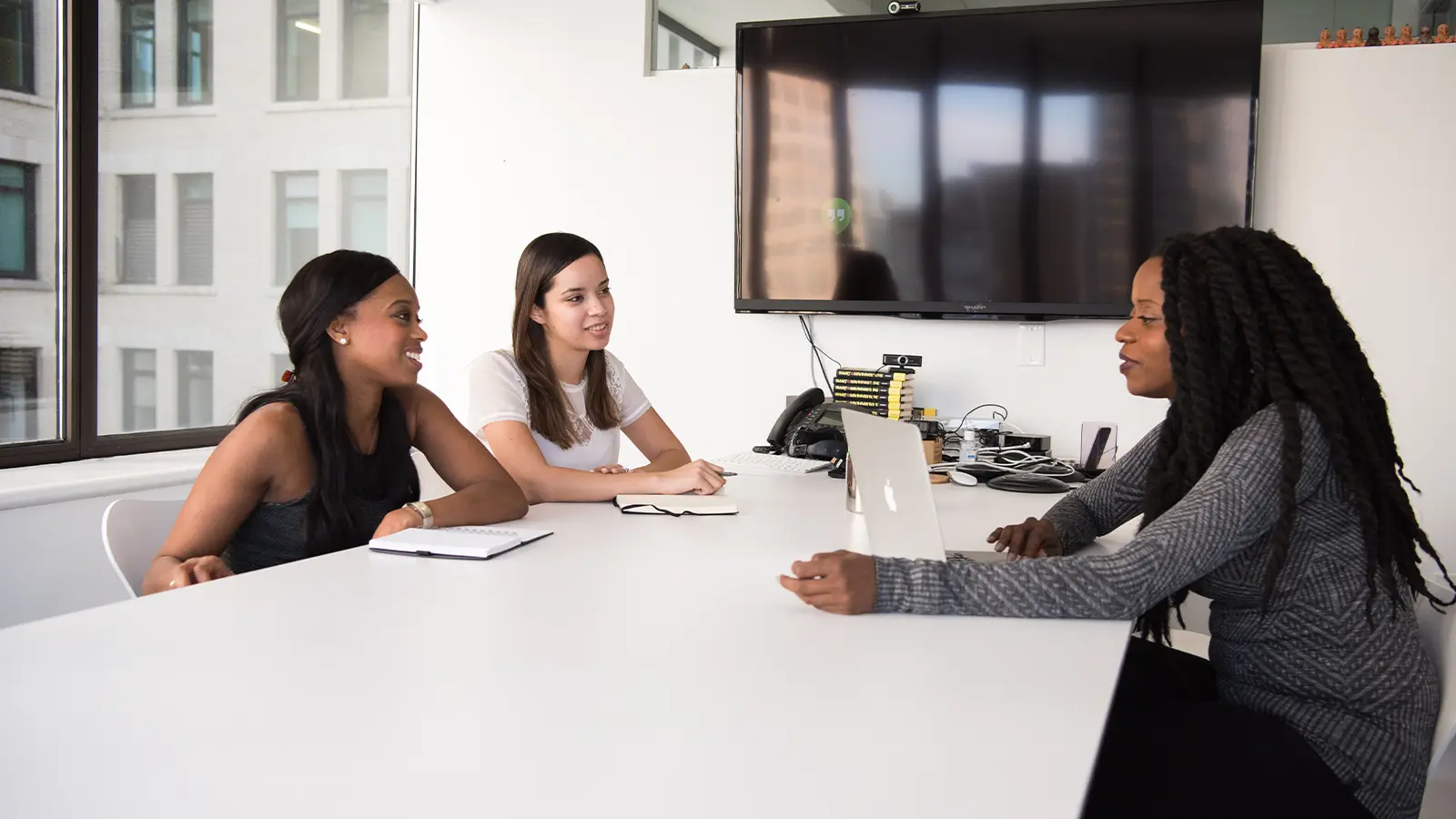 three women sitting down talking white table