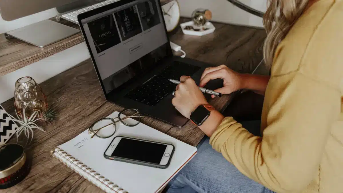 a remote worker typing on laptop with a notebook, glasses, and phone on desk