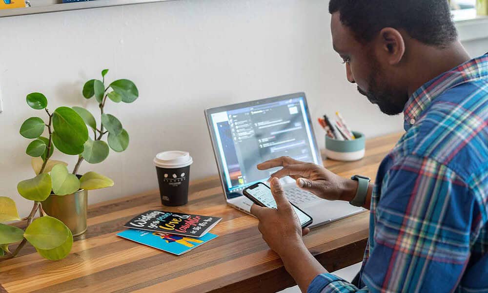 man looking at phone in front of his computer