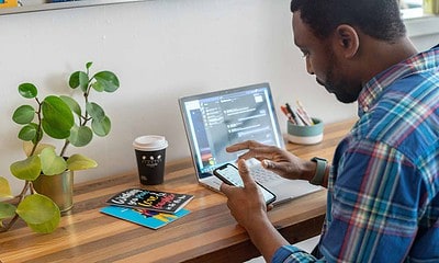 man looking at phone in front of his computer