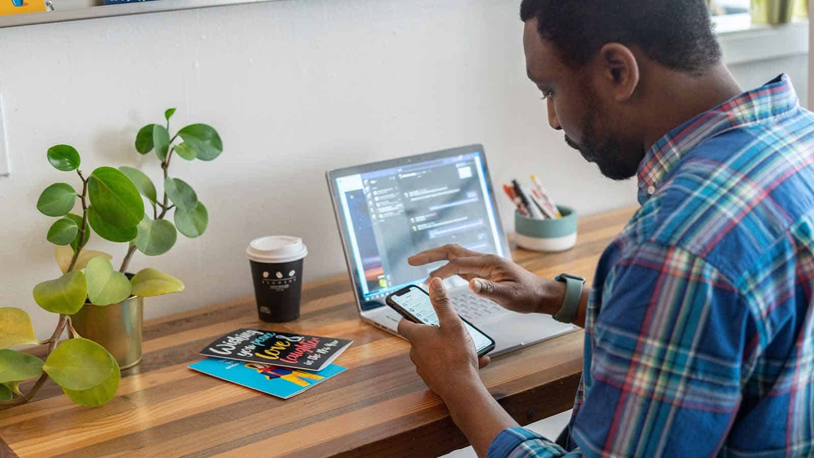 man looking at phone in front of his computer