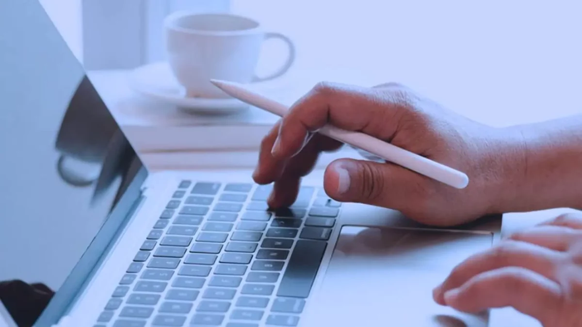 hands on laptop holding a pen