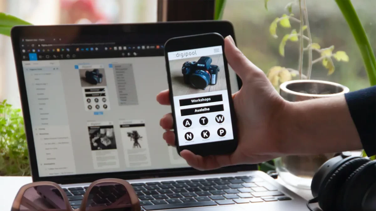 person holding a phone in front of a laptop showing a app being developed