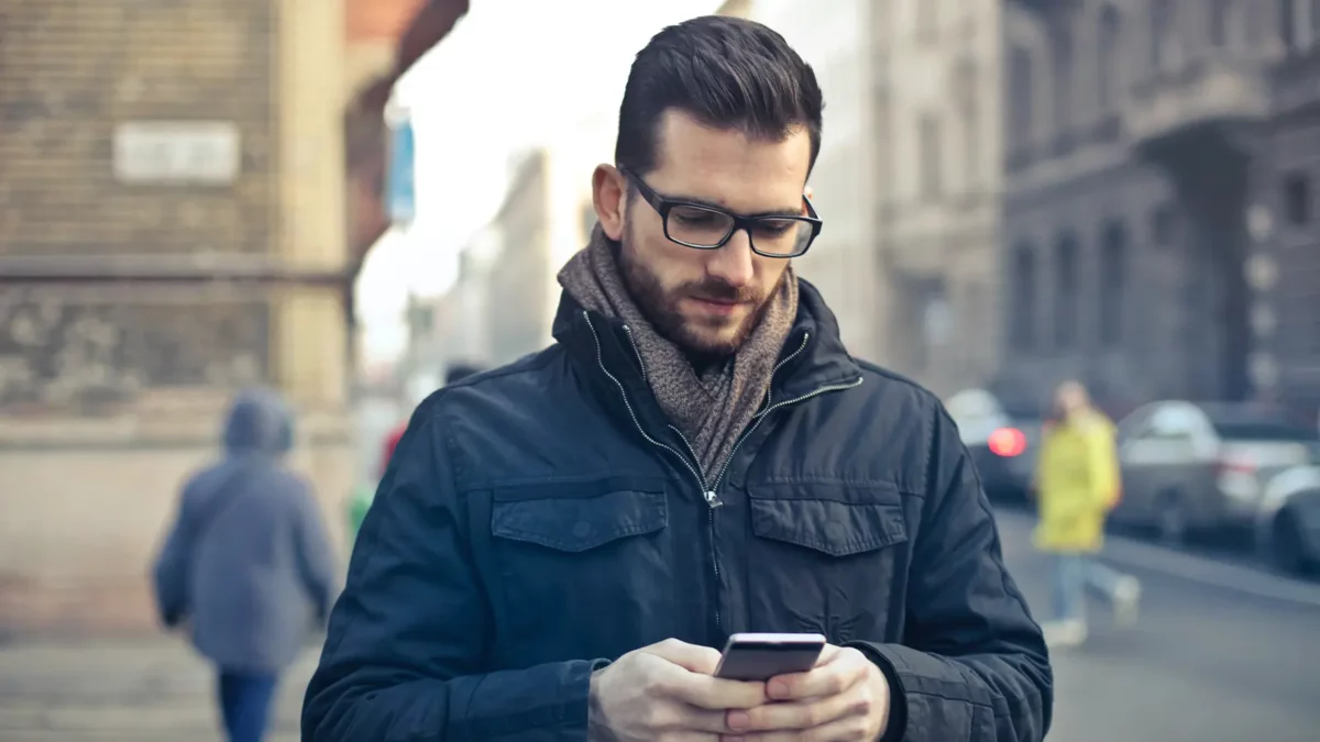 man looking down at his phone as he walks down a city street