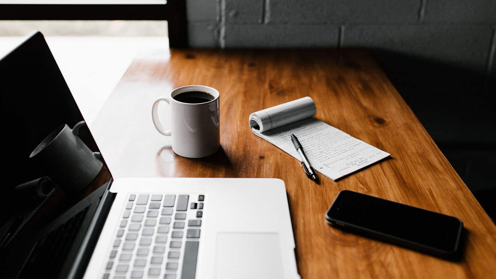 laptop on desk with a cup of coffee notepad and phone