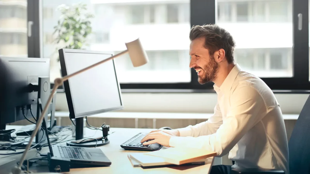 man sitting down typing on his computer and smiling