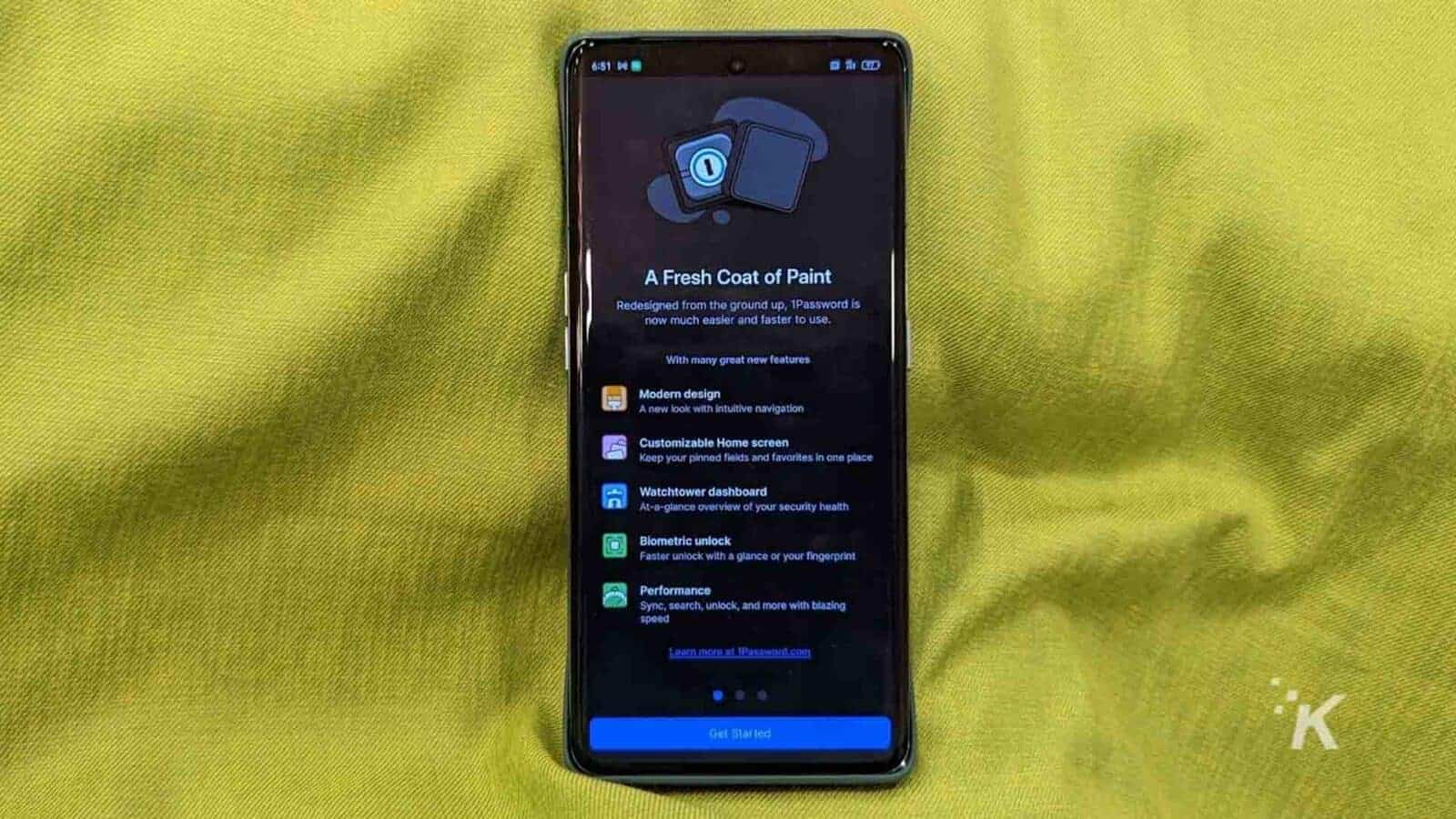 A smartphone displays a screenshot of the redesigned 1Password app with its modern design, intuitive navigation, customizable home screen, Watchtower dashboard, biometric unlock, and improved performance.