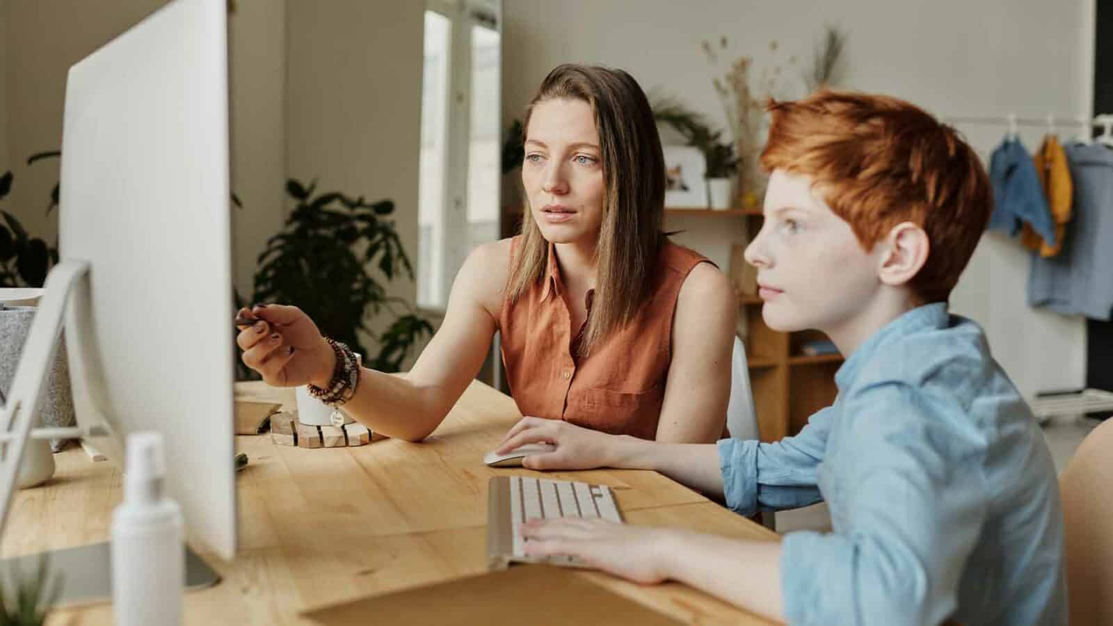 Two people sit at a table looking at a computer.