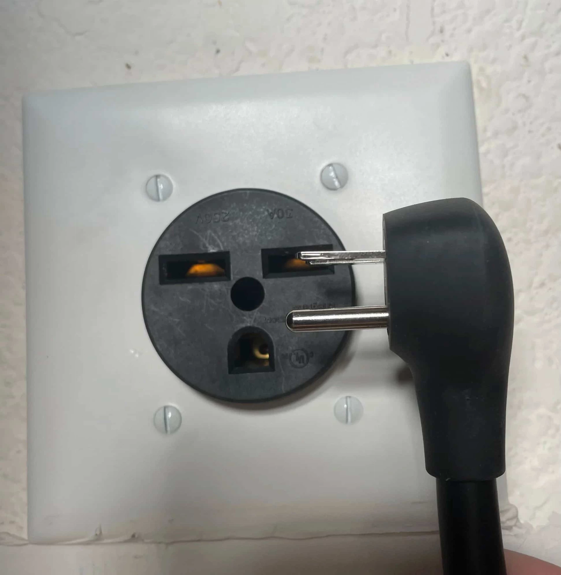 A person is holding a NEMA 14-50 adapter pointing it towards an indoor object they are holding.