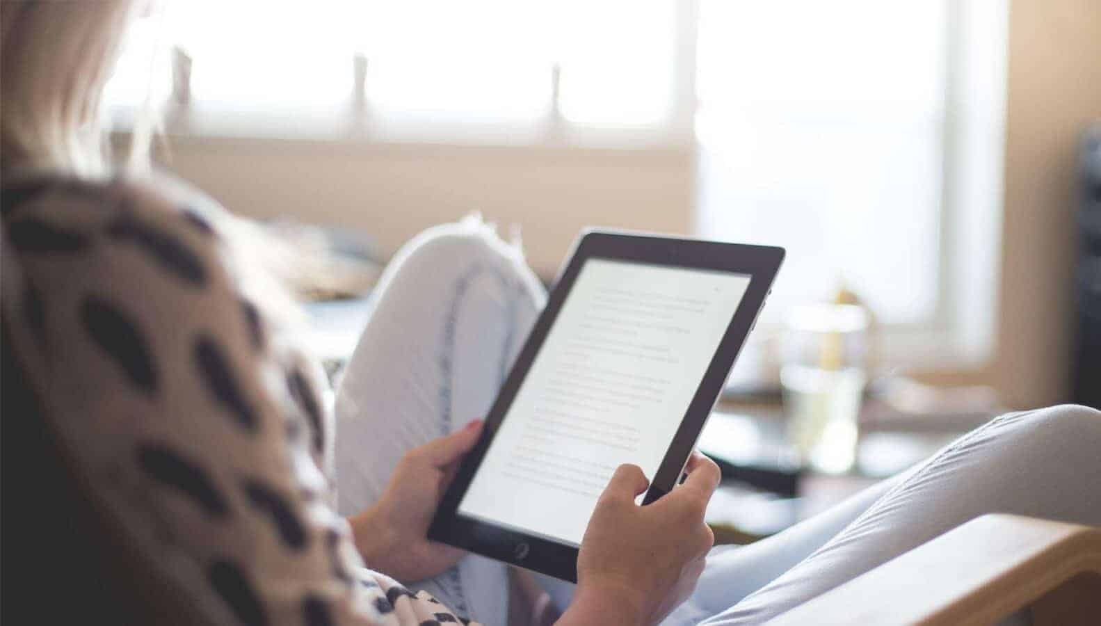 A person is reading a book while using a computer indoors.