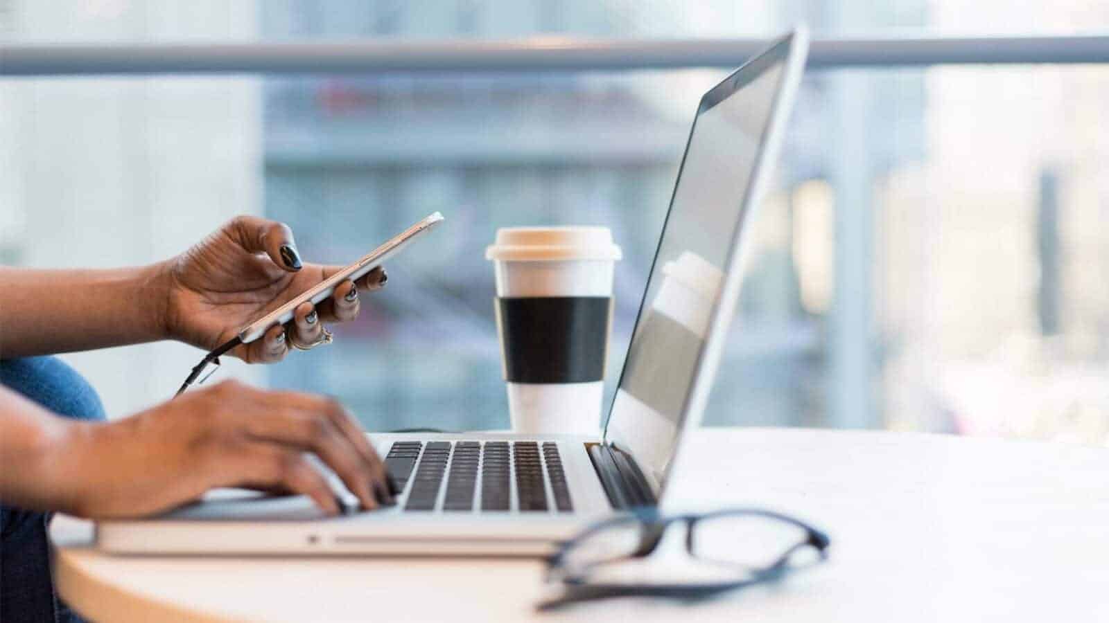 The person is using a laptop on a table while sipping a cup of coffee. Internal communication