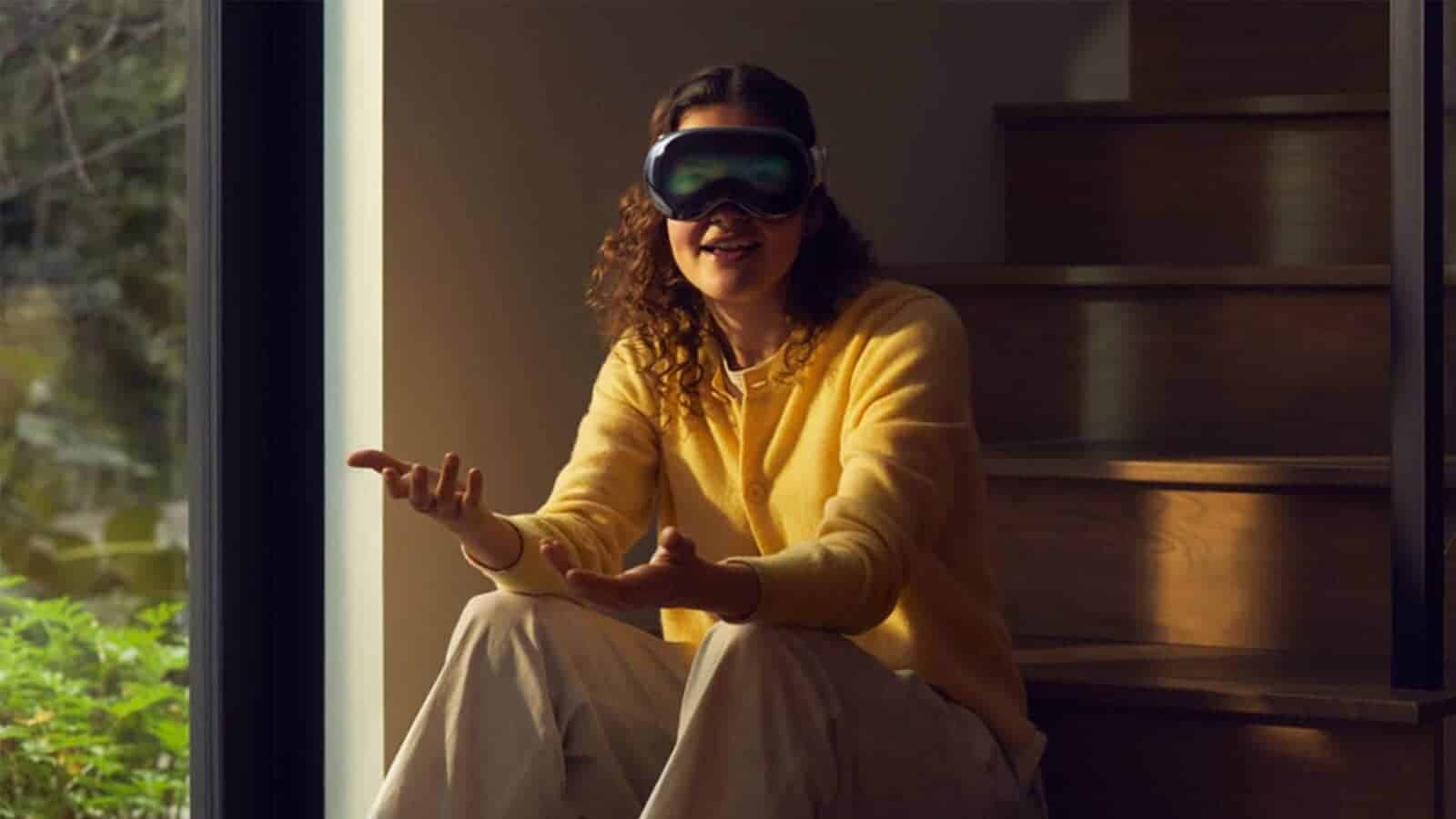 A person sits on a window sill wearing an Apple Vision Pro headset.