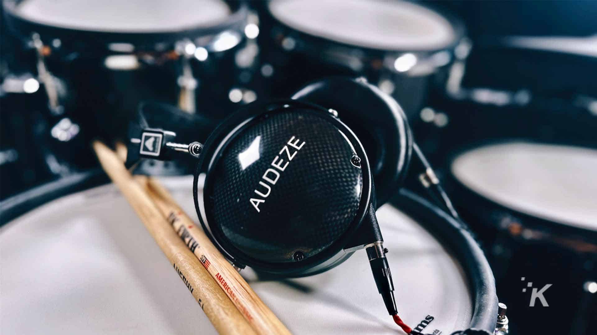 A drummer is playing a tom-tom drum, a membranophone percussion instrument, indoors with AUDEZE headphones.