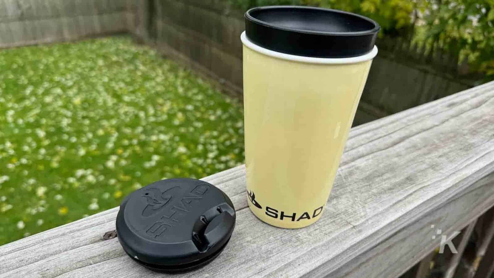The wooden surface holds a yellow cup with a lid and a black lid.