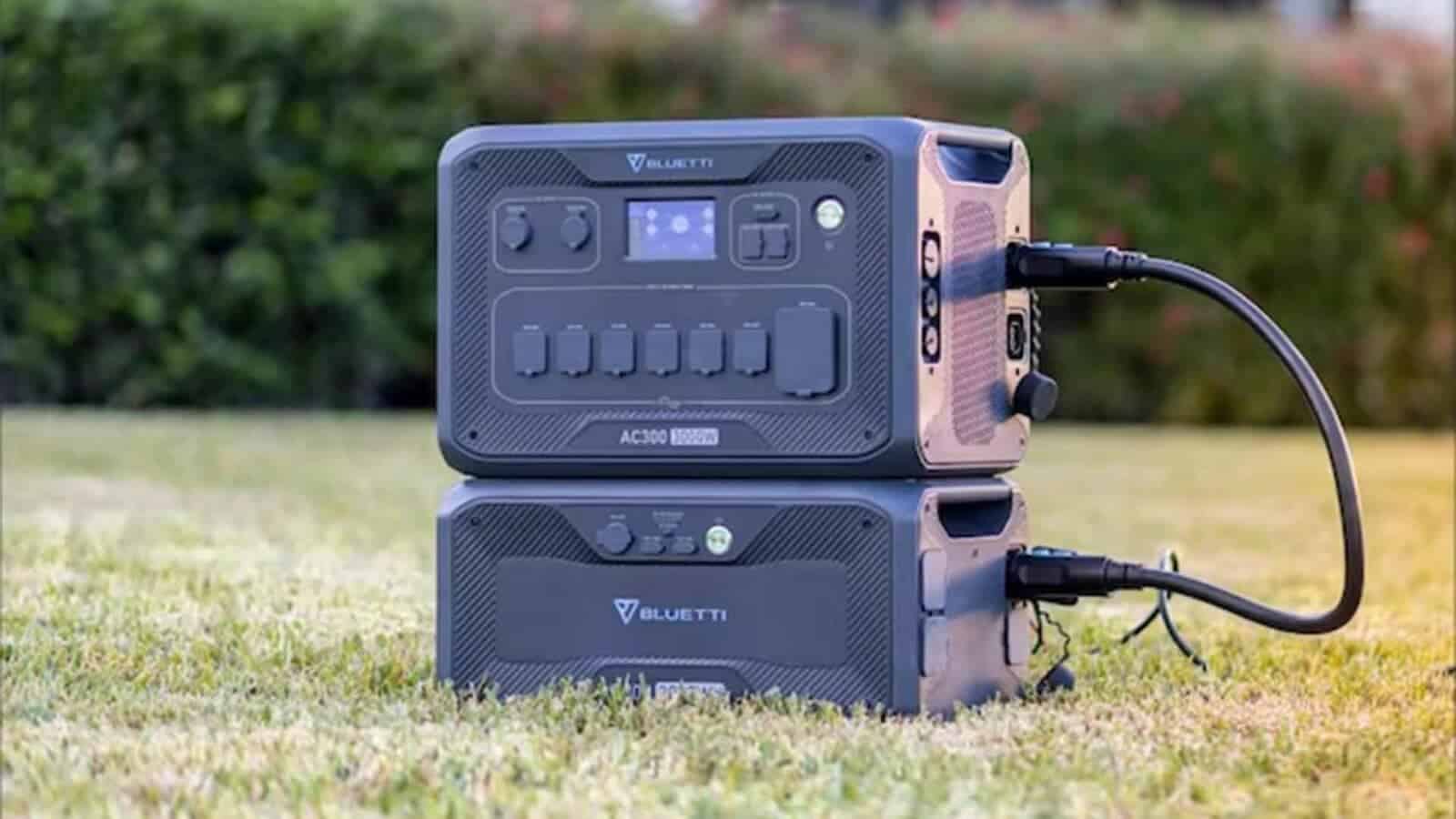 A BLUETTI portable power station with various outlets and a display screen, branded Bluetti, sits on grass with a blurred background of bushes.