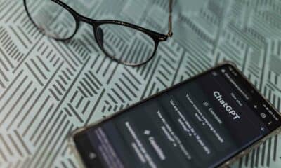 A smartphone with the ChatGPT app open lies on a patterned surface next to a pair of glasses, suggesting a work or study scenario.