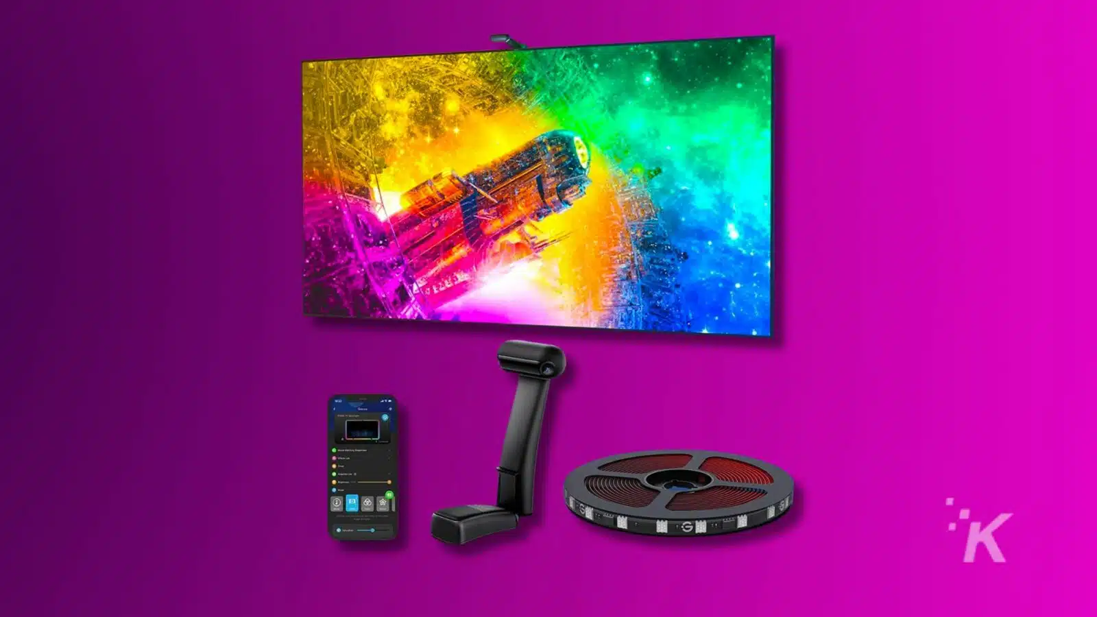 A vibrant ultrawide monitor displays colorful art above modern tech gadgets: a smartphone, webcam, and reel of LED strip lights, on a purple background.