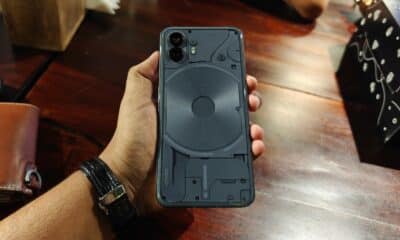A person is holding a smartphone with a transparent case, revealing its internal components and magnetic wireless charging coil, on a wooden table.
