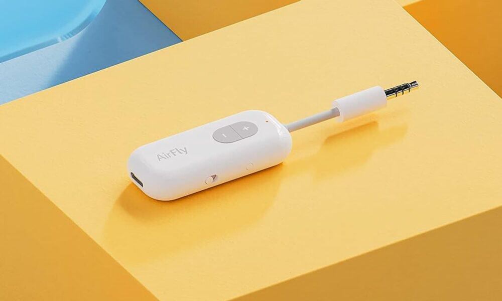 A white wireless twelve south headphone adapter with a plus and minus button lies on a dual-shade yellow background, with text "airfly" printed on its side.