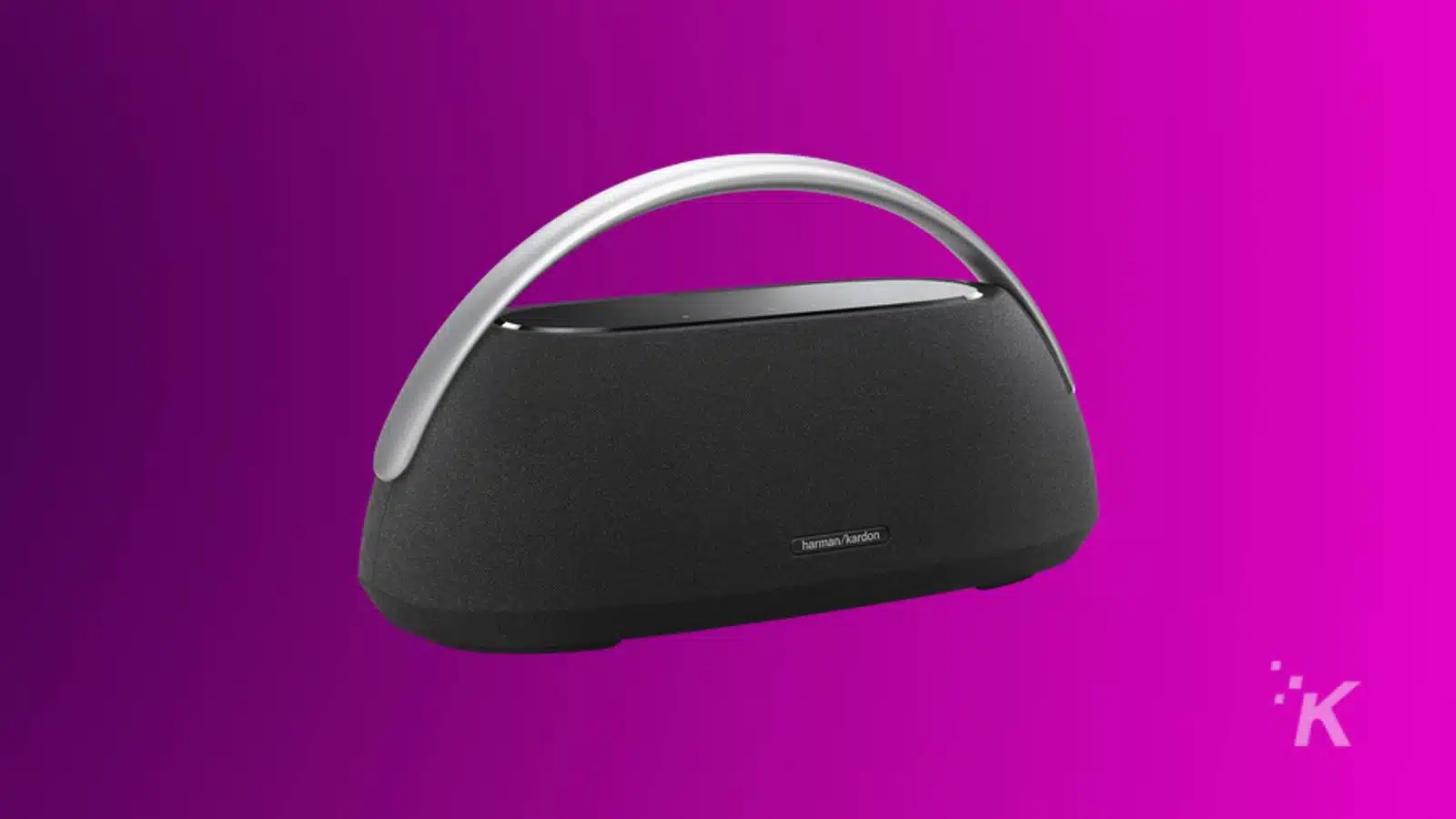 A Harman Kardon portable speaker with a sleek design, featuring a silver handle, on a purple background.