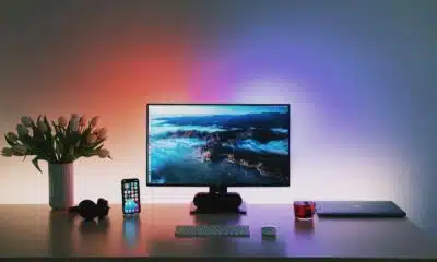 computer monitor on a desk with contrasting colored lighting on the wall behind