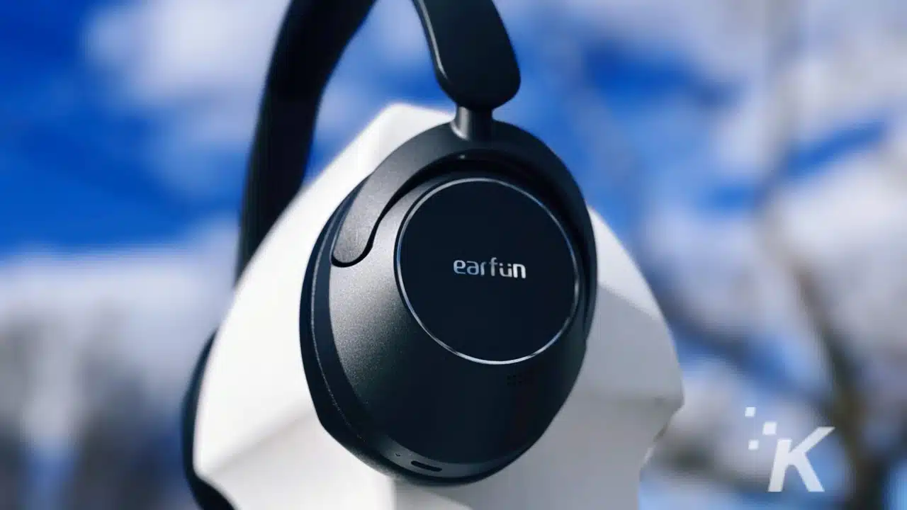 Close-up of EarFun branded over-ear headphone with blurred blue sky and clouds in the background.