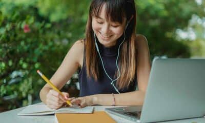 Woman writing on notepad with a laptop next to her.