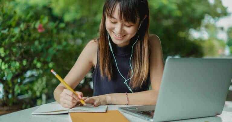 woman writing on notepad with a laptop next to her.