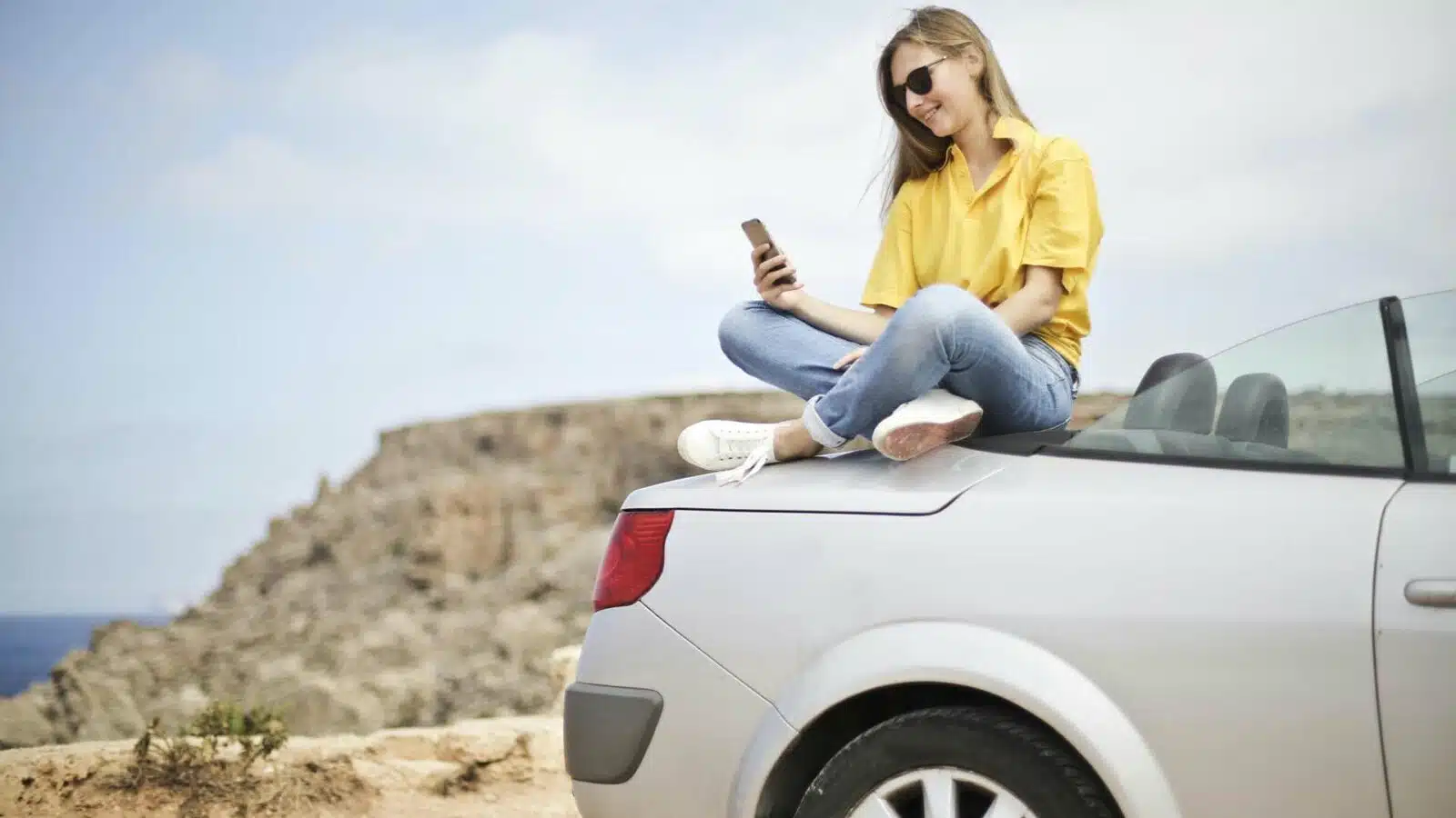 Woman using smartphone on car trunk outdoors