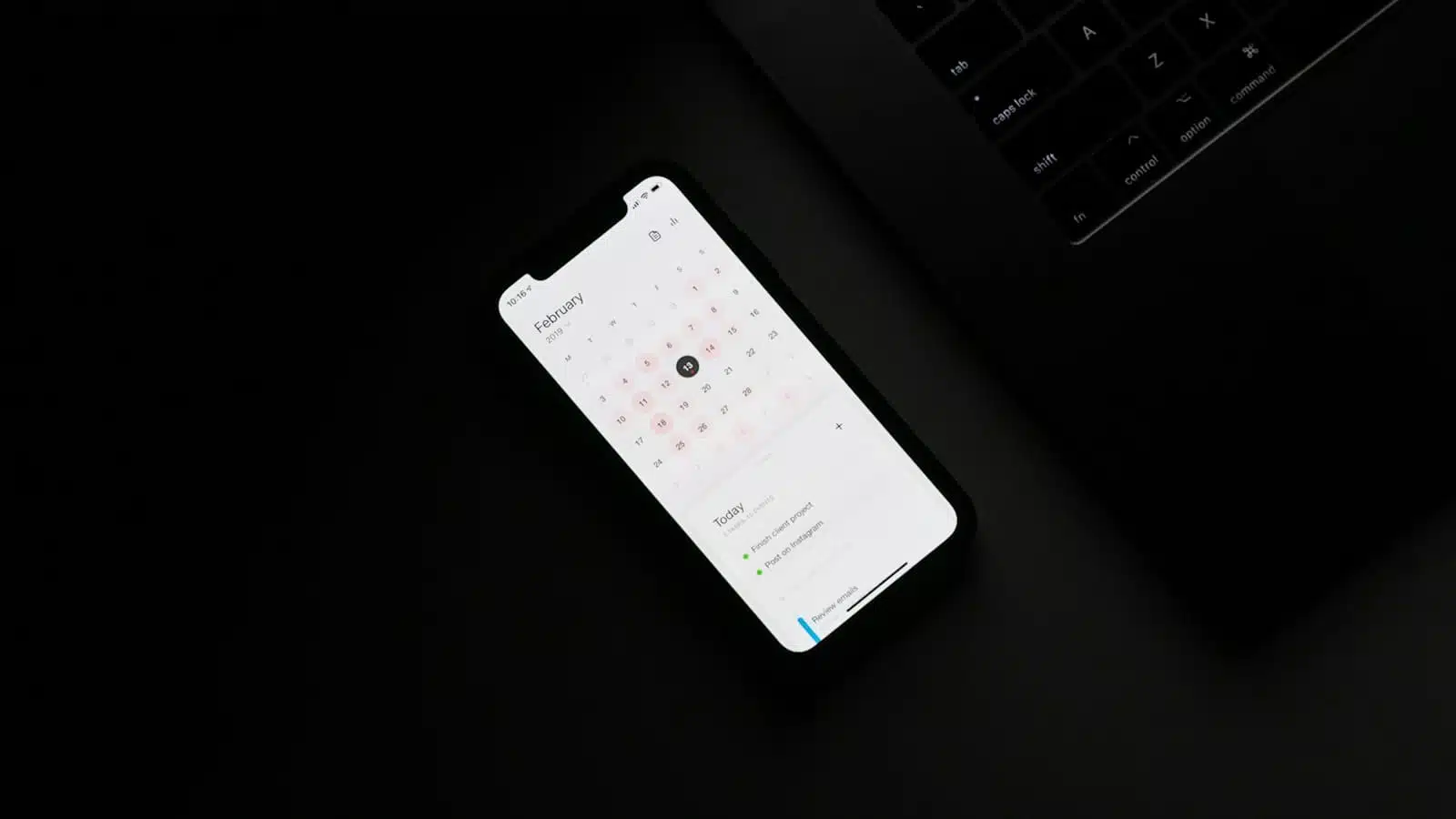 Smartphone calendar app open next to laptop.