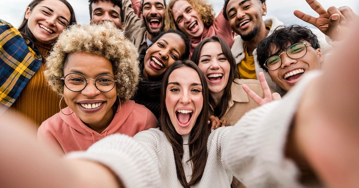Diverse group taking selfie, smiling together outdoors.