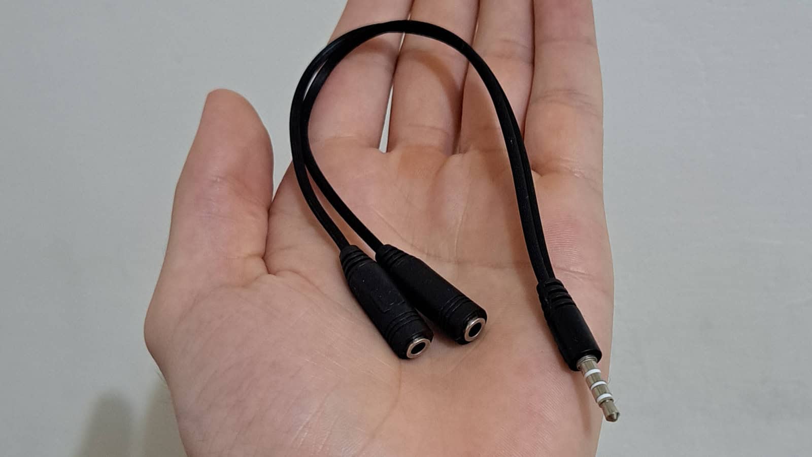 Hand holding audio splitter cable with dual jacks