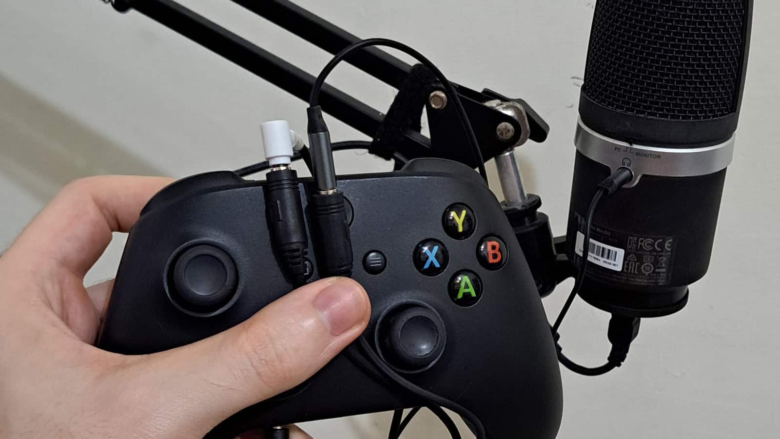 Hand holding controller and microphone with cables connected.
