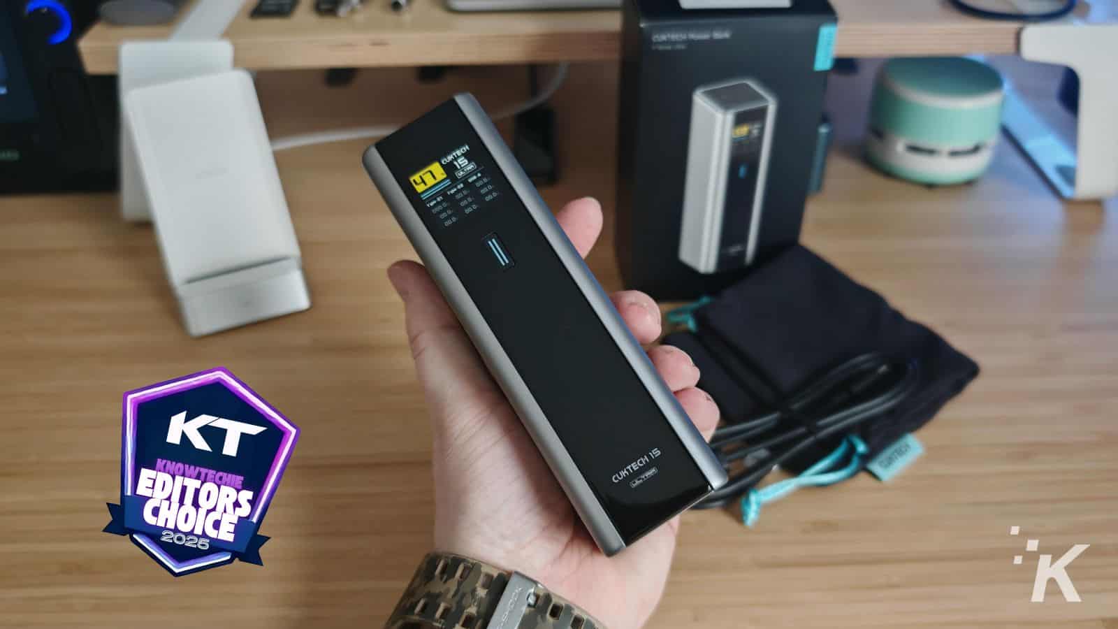 Hand holding portable battery power bank on desk.