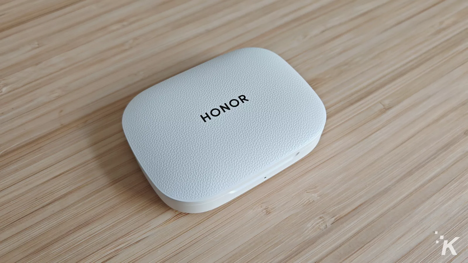 White Honor earbuds case on wooden surface