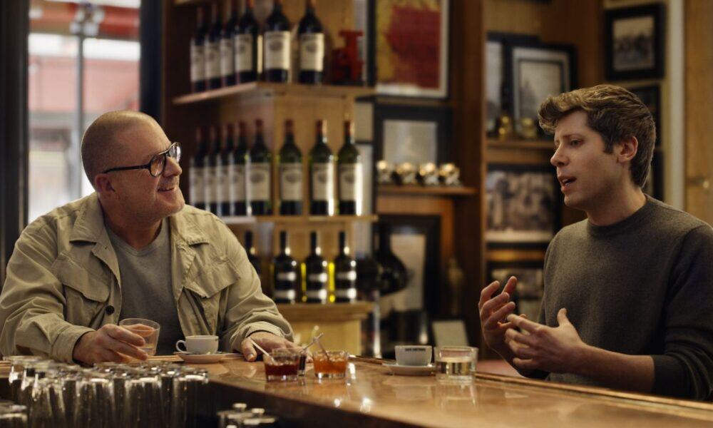 Two men talking in a bar with drinks.