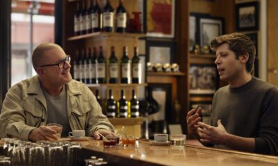 Two men talking in a bar with drinks.