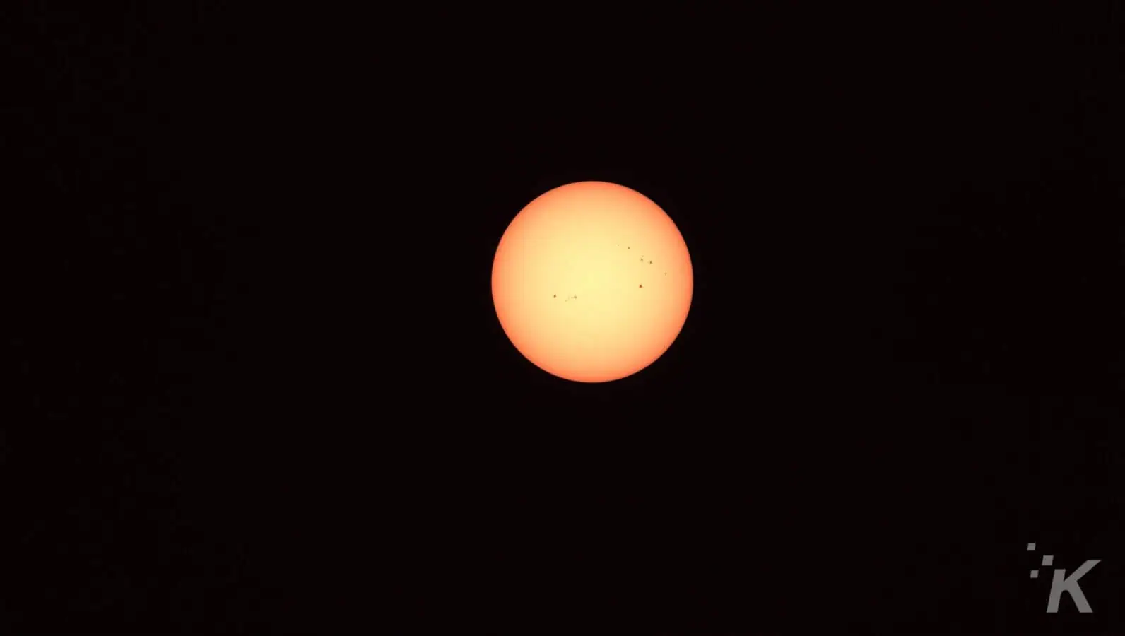 Bright sun with sunspots in dark sky.
