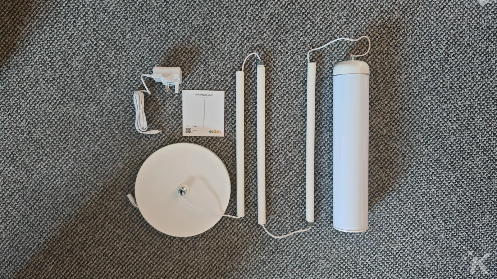 Smart LED floor lamp components on gray carpet.